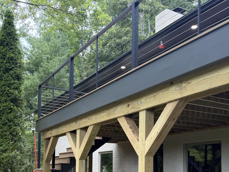 Elevated composite deck with black cable railing, timber posts, and the house behind